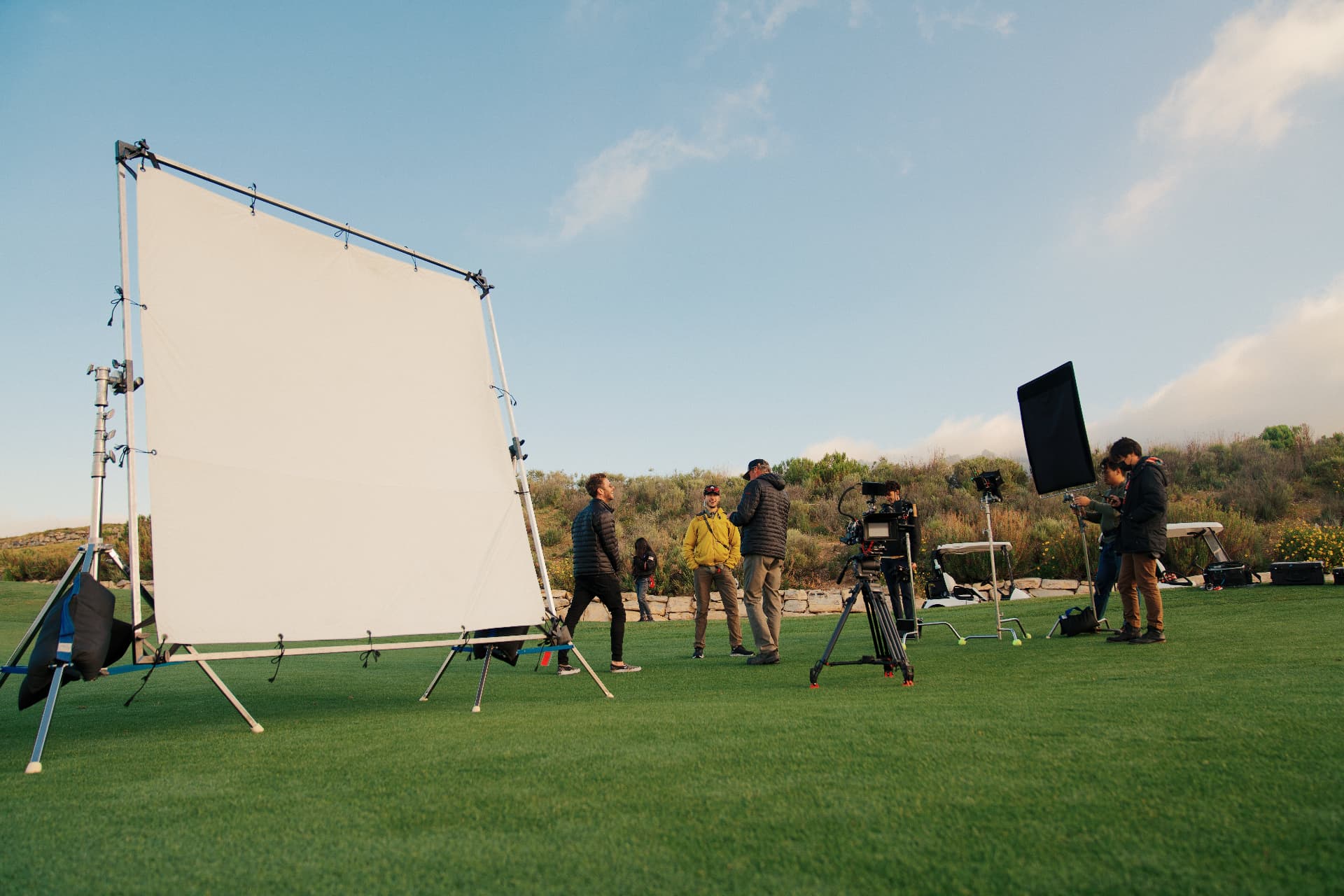 Film crew working beneath a large diffusion frame on a golf course